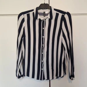 Svartvit randig skjorta från H&M Divided - Snygg svartvit randig skjorta från H&M Divided i storlek 36. Skjortan har långa ärmar och knappar framtill. Perfekt för en stilren look.