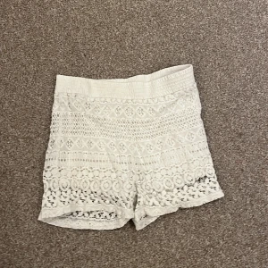 Vita spets shorts - Snygga vita shorts i spets med hög midja. Perfekta för sommarens varma dagar. De har ett vackert mönster och en elastisk midja för extra komfort.