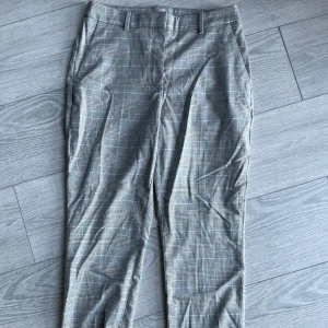 Rutig kostymbyxa från H&M - Snygga kostymbyxor från H&M i ett klassiskt rutigt mönster. Byxorna har en normal passform och är perfekta för en stilren look. De har hällor för bälte och en diskret dragkedja framtill.