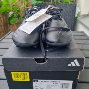 Nya svarta fotbollsskor Adidas Copa Pure 2 Club - Säljer ett par svarta Adidas Copa Pure 2 Club fotbollsskor. Skorna har en stilren design med snörning och är tillverkade i syntetmaterial. Perfekta för spel på fasta underlag. Har aldrig använts.