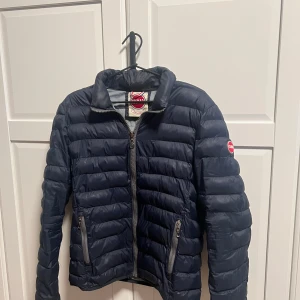 Mörkblå pufferjacka från Colmar - Säljer en snygg mörkblå pufferjacka från Colmar. Jackan har en dragkedja framtill och långa ärmar. Perfekt för kyligare dagar med sin quiltade design. Den har en klassisk look med en liten logga på ärmen. Priset går att diskutera med en snabb affär. Svarar snabbt🙌