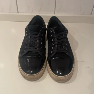 Svarta sneakers från Lanvin - Snygga svarta sneakers från Lanvin med en stilren design. Skorna har en glansig yta och klassisk snörning. Perfekta för en avslappnad men ändå elegant look. Priset går att diskuteras. Skor, dustbag följs med. Skriv vid några funderingar 🤩🌟