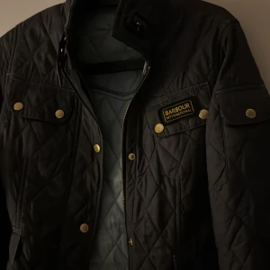 Barbour - Säljer en stilren svart quiltad jacka från Barbour med guldknappar och flera fickor. Jackan har en hög krage och är perfekt för kyligare dagar. Den har en klassisk design med en snygg passform. Perfekt inför vår och sena sommar kvällar , kostade: 4700kr köpt på hanzens förra året på våren så knappt använd. 