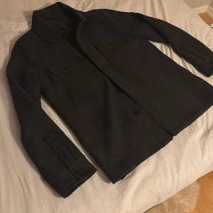 Mörkgrå overshirt med knappar - Snygg mörkgrå overshirt med knappar framtill och två bröstfickor. Perfekt för lager-på-lager-stil. Den har långa ärmar och en klassisk krage.