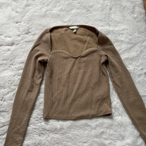 Beige ribbad topp - Säljer en beige ribbad topp med långa ärmar och en v-ringad design. Perfekt för en stilren och bekväm look. Passar bra till både jeans och kjol. Köpt för 200kr säljer för 100kr har endast haft på mig 3 gånger under året jag haft den