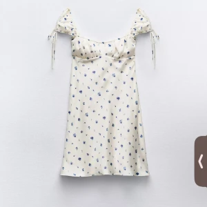 Vit blommig klänning - Söt vit klänning med blå blommor och knytband vid axlarna. Den har en smickrande passform och kort längd, perfekt för varma dagar. Köpte 2 storlekar, så helt ny med prislapp!