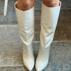 Vita stövlar med spetsig tå - Snygga vita stövlar med spetsig tå och klack. De har en elegant och stilren design med en lätt textur på ytan. Perfekta för att lyfta vilken outfit som helst.