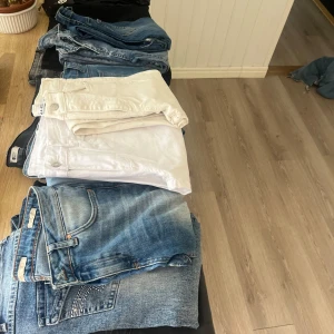 Samling av jeans och vita byxor - En samling av jeans i olika blå nyanser och vita byxor. Perfekt för den som vill ha variation i garderoben. Jeansbyxorna har klassiska detaljer och olika tvättar, medan de vita byxorna ger en fräsch look.