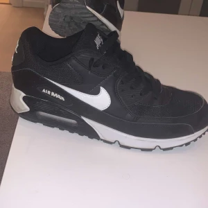 Svarta Nike Air Max sneakers - Snygga svarta Nike Air Max sneakers med vit sula och vit swoosh-logga. Skorna har en klassisk design med snörning och är perfekta för en sportig look.