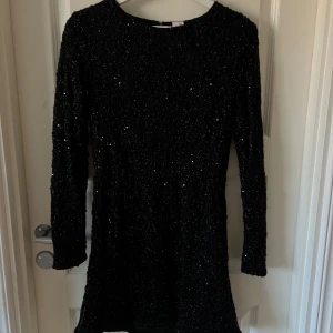 Svart glittrig klänning - Snygg svart klänning med glittriga paljetter som ger en festlig look. Jättefint skick, använd en gång. Liten i strlk.