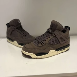 Jordan 4  - Säljer ett par bruna sneakers från Nike med en unik design. Skorna har snörning och en robust sula med Nike-logga. Perfekta för dig som vill ha en stilren look med en twist.