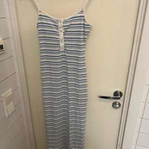 Randig långklänning med knappar - Säljer en somrig långklänning med blå och vita ränder. Klänningen har smala axelband och knappar framtill. Perfekt för varma dagar! Otroligt skön. Lite nipprig men inget man störs av. 