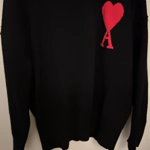Ami Paris tröja  - Snygg svart ami Paris tröja med ett rött hjärta och bokstaven 'A' på bröstet. Perfekt för en stilren look med en touch av kärlek. Tröjan har långa ärmar och en klassisk passform. Storlek S och sitter fint.