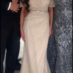 Champagnefärgad långklänning med volangärm och bälte - Säljer en elegant champagnefärgad långklänning med omlottliv, korta volangärmar och markerad midja med bälte. Klänningen har ett diskret prickigt mönster och v-ringning, perfekt för speciella tillfällen.