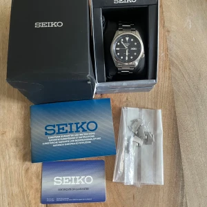 Seiko 5 sport  - Säljer en Seiko 5 automatisk klocka i silver med svart urtavla och dag/datumvisning. Klockan har rostfritt stålarmband och transparent baksida som visar urverket. Originalask, extra länkar och garantikort medföljer. Klockan är köpt hos uret.se för 3200. Tveka inte på att skriva om ni har några frågor