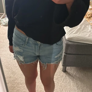 Ljusblå jeansshorts med fransar och slitningar - Säljer ett par ljusblå jeansshorts med råa fransar och slitna detaljer framtill och på sidorna. Storleken är M men skulle mer säga det är en S.