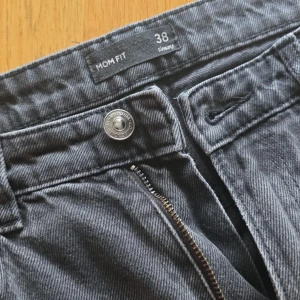 Grå mom fit jeans - Säljer ett par grå mom fit jeans i storlek 38. Byxorna har klassisk femficksdesign, dragkedja och knapp framtill. Perfekta för en avslappnad och trendig look.
