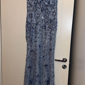 Ljusblå långklänning med paljetter - Säljer just nu en ljusblåa långklänningar, med glittriga paljetter och korta ärmar. Klänningen har en figurnära passform och vackra detaljer över hela tyget som ger en lyxig känsla. Perfekt för bal eller festliga tillfällen.  Endast använd vid ett tillfälle, finns i storlek S/M & M/L 