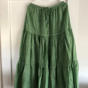 Grön långkjol från ZARA med knyt - Säljer en luftig grön långkjol från ZARA i linneblandning. Kjolen har resår i midjan och dekorativt knytband med pärldetaljer. Perfekt för varma dagar och enkel att styla med olika toppar.