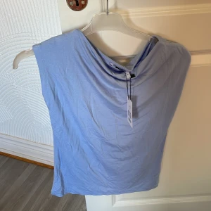 Ljusblå ärmlös topp med draperad hals - Säljer en ljusblå ärmlös topp med snygg draperad halsringning. Tags kvar! Perfekt för dig som vill ha en enkel men stilren look. Mjuk och skön i materialet, passar till många olika outfits. Storlek s.  50kr .. säljer även i rosa
