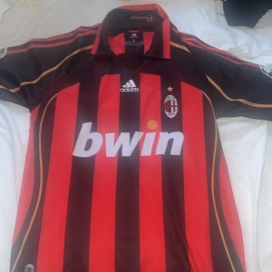 AC Milan fotbollströja Maldini #3.. RETRO - Säljer en klassisk AC Milan matchtröja från Adidas med Maldini och nummer 3 på ryggen. Tröjan är röd och svart med vertikala ränder, gulddetaljer och klubbmärke broderat på bröstet. Kortärmad modell med sponsortryck på framsidan.