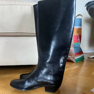 Svarta skinnstövlar med spetsig tå - Säljer ett par klassiska svarta stövlar i skinn med spetsig tå och låg klack. Stövlarna har en stilren design med diskreta mönsterdetaljer framtill och passar perfekt till många olika outfits.