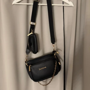 Svart axelväska från Juicy couture  - Snygg svart axelväska från Juicy couture med guldfärgade detaljer och kedja. Väskan har justerbar axelrem och ett extra litet fack framtill. Perfekt för att bära det viktigaste med stil.