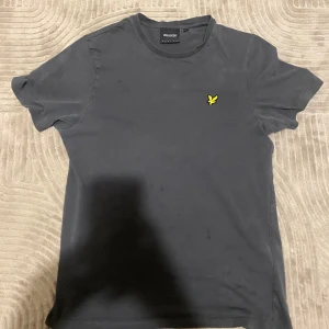 Svart t-shirt från Lyle & Scott - Säljer en svart t-shirt från Lyle & Scott med klassisk passform. T-shirten har korta ärmar och en gul broderad logga med fågel på bröstet. Perfekt till vardags och enkel att matcha med andra plagg. Pris går att diskuteras