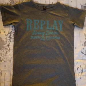 Grå t-shirt från Replay - Säljer en grå t-shirt från Replay med blå texttryck på bröstet och korta ärmar. 