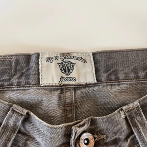 Grå jeans från Tiger of Sweden - Säljer ett par grå jeans från Tiger of Sweden med klassisk femficksdesign och knappgylf. Jeansen har raka ben och normal passform, perfekta till vardags. Snygga detaljer med Tiger of Sweden-logga på fickan.