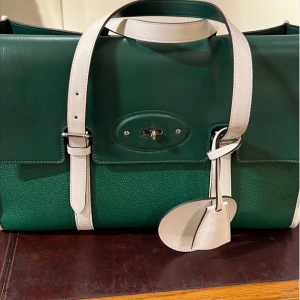 Grön och vit handväska med detaljer - Snygg handväska i mörkgrönt skinn med vita handtag och remmar. Väskan har silverfärgad låsdetalj framtill och en matchande vit tag. Perfekt storlek för att bära med sig det viktigaste och ger en stilren look.