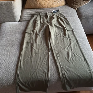 Olivgröna cargopants från Hollister - Säljer ett par olivgröna cargopants från Hollister med raka ben och stora fickor på sidorna. Byxorna har hög midja och är perfekta för en avslappnad stil. Supersnygga till sneakers eller boots!