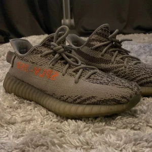 Adidas Yeezy Boost 350 V2 Beluga - Säljer ett par Adidas Yeezy Boost 350 V2 Beluga med grå och orange detaljer. Skorna har stickad ovandel, snörning och en bekväm, ribbad sula. Perfekta för dig som vill ha en unik sneaker med streetkänsla.