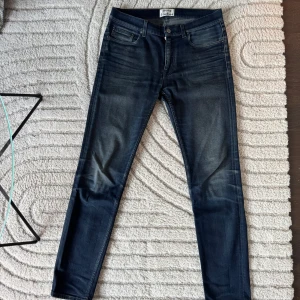 Mörkblå jeansbyxor från Acne Studios - Säljer ett par mörkblå jeans från Acne Studios, modell Ace Oreo. Byxorna har klassisk femficksdesign, smal passform och normal midja. Snygga slitningar och diskret tvätt för en modern look. Perfekta till vardags eller när du vill vara extra stilig. Storlek 31/32, men något liten i storleken.