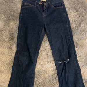 Blå jeansbyxor från gina perfect jeans - Mörkblå jeansbyxor från gina perfect jeans med klassisk femficksdesign och orangea sömmar. Byxorna är boot cut och har en bra passform och ett hål med slitning på ena benet för en trendig look. Perfekta för dig som gillar en avslappnad stil.