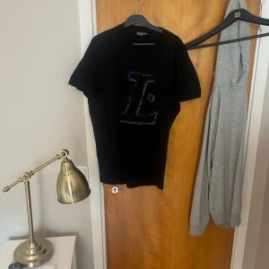 Lanvin T-shirt - Säljer en svart t-shirt från Lanvin med ett stort tryck i blått och vitt på bröstet. T-shirten har klassisk passform och rund hals. Perfekt för dig som gillar stilrena plagg.