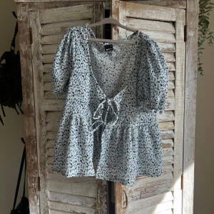 Blommig blus med puffärm från Gina Tricot - Supersöt blus från Gina Tricot med blått blommönster på vit botten. Blusen har puffärmar, v-ringning och knyt framtill. Perfekt för sommarens alla tillfällen!