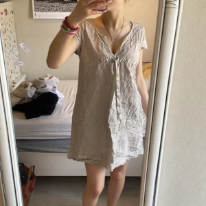 Beige kortklänning med knyt från Odd Molly - 60kr Supersöt beige kortklänning från Odd Molly med knyt framtill och lätt struktur i tyget. Klänningen har korta ärmar och v-ringning, perfekt för varma dagar. Enkel och stilren design som passar till många tillfällen.