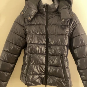 Svart pufferjacka med huva från lager 157 - Säljer en svart pufferjacka med avtagbar luva. Säljer då den inte längre kommer till användning. Väldigt bra skick. Från lager 157.