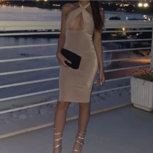 Beige omlottklänning med halterneck - Säljer en beige, figurnära klänning med omlottdesign och halterneck. Klänningen har en öppen rygg och en snygg cut-out framtill. Perfekt för sommarkvällar eller festliga tillfällen. Matcha med klackar och en liten väska för en komplett look.