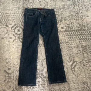 Mörkblå jeansbyxor från Aigle Denim - Säljer ett par klassiska mörkblå jeansbyxor från Aigle Denim med raka ben och kontrastsömmar. Byxorna har fem fickor och en snygg broderad detalj på bakfickorna. Perfekta för en stilren vardagslook.