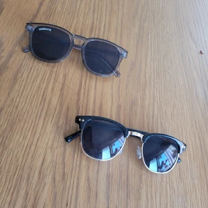 Två par solglasögon - Säljer två par snygga svarta solglasögon. Ena paret är från Bonrito med transparenta skalmar och klassisk rundad form. Det andra paret har en mer markerad båge med silvriga detaljer vid gångjärnen och näskuddar för extra komfort.