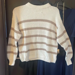 Vit och beige randig stickad tröja från 157 - Säljer en stickad tröja från 157 i storlek S. Tröjan är vit med breda beigea ränder, har rund halsringning och långa ärmar. Perfekt för lager-på-lager och en avslappnad stil, och har används fåtals gånger.