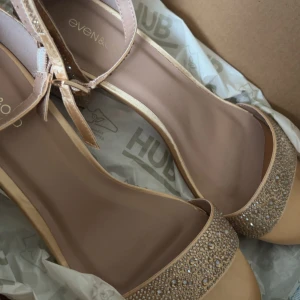 Beige sandaler med glittriga detaljer från Even&Odd - Säljer ett par snygga beige sandaler från Even&Odd med glittriga stenar på remmen över tårna. Skorna har en öppen tå och justerbar rem runt vristen. Perfekta för att lyfta din outfit med lite extra bling.