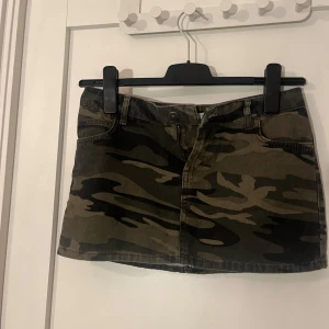 Camo minikjol från Subdued - Snygg camouflagefärgad minikjol från Subdued med klassisk femficksdesign och dragkedja framtill. Kjolen är i jeansmaterial och har coola gröna och svarta toner. Aldrig använd då den var för liten på mig.