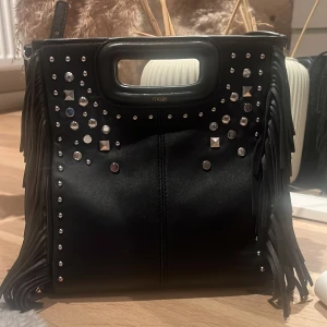 Svart axelväska med nitar från Maje - Väska från Maje. Knappt använd inga defekter, köpt i Italien för 2 år sen för 3200kr. Jätte fin o rymmer mycket.