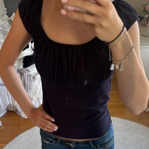 Topp brandy Melville - Supersöt mörkblå topp från Brandy Melville med puffiga korta ärmar och rynkad urringning. Sitter tajt och har en feminin siluett. Gjord i mjuk bomull med lite elastan för extra stretch. Perfekt till jeans eller kjol för en trendig look.