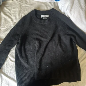 Svart stickad tröja från Notshy - En svart stickad tröja från Notshy med rund halsringning och långa ärmar. Tröjan har breda ribbade muddar vid ärmslut och nederkant, vilket ger en snygg och enkel look. Perfekt för lager-på-lager under kyliga dagar.