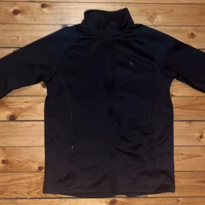 Svart vindjacka (158-164) - *Priset kan diskuteras*  Svart vindjacka med hel dragkedja framtill, hög krage och diskret logga på bröstet. Jackan har långa armar med tumhål och två fickor med dragkedja. Perfekt för dig som gillar en clean och sportig look. Är mycket bra för utomhus sporter när det blir kyligare. Storlek passar 11-12 år gammal pojke eller 13-15 år gammal flicka.