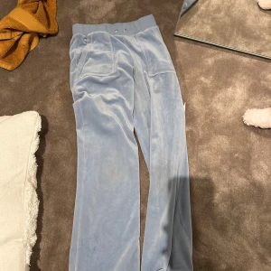 Ljusblå velourbyxor Juicy Couture XXS - Supermjuka ljusblå velourbyxor från Juicy Couture i storlek XXS. Byxorna har bred resår i midjan, raka ben och stora fickor framtill. Perfekta för en chill och trendig look. Har inte snörerna